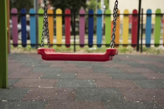 Swinging cradle for children in park. Playing concept. Fence painted in rainbow colors.