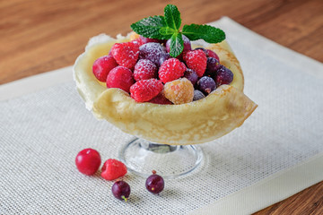 Fresh berries sprinkled with powdered sugar and wrapped in a pancake, which lie in a vase on the table.