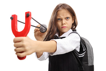 Angry little schoolgirl aiming with a stone and a slingshot