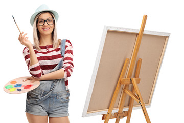 Young woman with a paintbrush and a color palette next to an easel