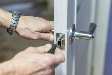 man repairing the doorknob with screwdriver. worker's hand installing new door locker