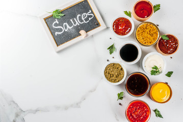 Set of different sauces - ketchup, mayonnaise, barbecue, soy, teriyaki, mustard, grain hills, pesto, adzhika, chutney, tkemali, pomegranate sauce on white marble background. Top view copy space