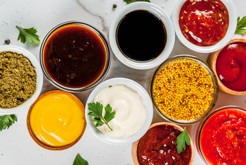 Set of different sauces - ketchup, mayonnaise, barbecue, soy, teriyaki, mustard, grain hills, pesto, adzhika, chutney, tkemali, pomegranate sauce on white marble background. Top view copy space