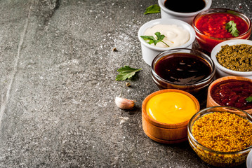 Set of different sauces - ketchup, mayonnaise, barbecue, soy, teriyaki, mustard, grain hills, pesto, adzhika, chutney, tkemali, pomegranate sauce on black stone background. Copy space