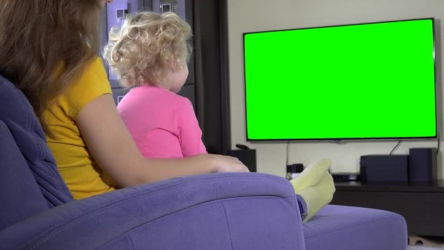 little kid watching TV program with mom. Green chroma key screen