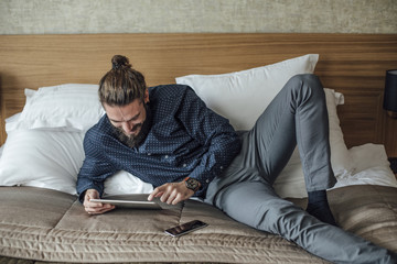 Man Lying on Bed and Reading on Tablet