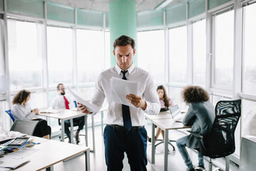 Skilled managers in white shirt reading documents by standing at his desk. Office concept.