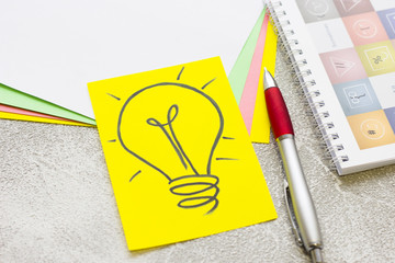 New Idea Inspiration Business Concept with an image of a yellow light bulb, notebook and paper, close up, grey concrete background