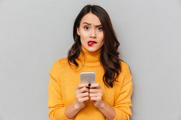 Worried brunette woman in sweater with smartphone bites her lip