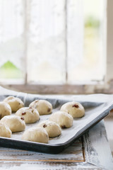Raw unbaked buns. Ready to bake homemade Easter traditional hot cross buns on oven tray with baking paper over white wooden table with window at background. Natural day light. Rustic style.