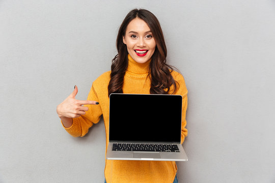 Happy brunette woman in sweater showing blank laptop computer screen