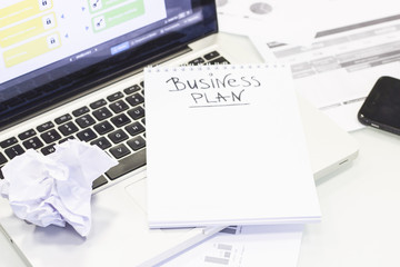 Fototapeta premium Business, Finance, Analysis concept. A workplace with a laptop, a crumpled paper ball and a Business Plan inscription in a blank notebook