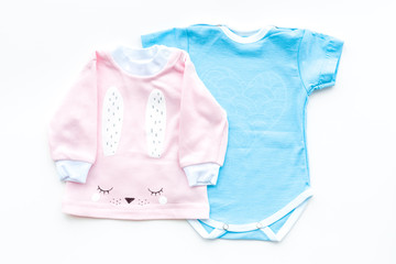 Baby clothes concept. Blue bodysuit for boy and pink shirt for girl near baby accessories on white background top view