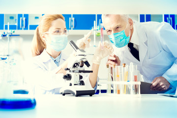 Supportive relations. Laboratory coworkers wearing masks while cooperating over an experiment and examining test tubes with different liquids.