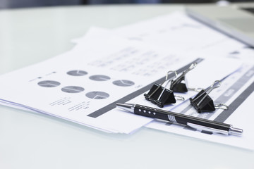 Business Office Workplace Concept. A close up of black paper clips and a pen on printed graphs and charts