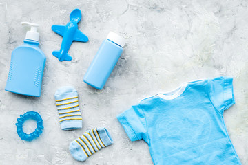 Fototapeta na wymiar Blue set for newborn boy. Baby bodysuit, socks, airplan toy, soap and powder on grey background top view