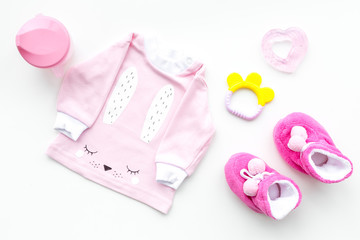 Obraz na płótnie Canvas Cute pink baby clothes for girl. Shirt, booties, toy, bottle on white background top view copy space