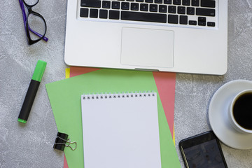 Modern office table desk, flat lay, top view. Businessman workplace with a laptop, glasses, coffee cup, black smartphone and notepad, grey concrete background, copy space