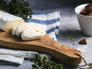 Close-up of camembert cheese on the wooden cutboard with pecan nuts and thyme.