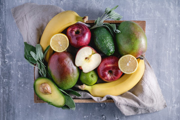 Top view of fresh fruits in the wooden box on the textured blue background.