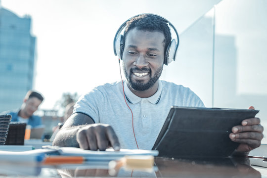 Education is the key to success. Low angle shot of a cheerful college guy smiling while enjoying the music playing in his headphones and working on a home assignment.