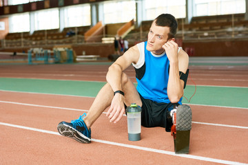 Full length portrait of young amputee athlete sitting on running track taking break from practice  to relax and listen to music, copy space