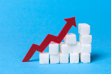 Increase the sugar content in the cow. Diabetes. Stair of sugar cubes and a red arrow up on a blue background. - obrazy, fototapety, plakaty
