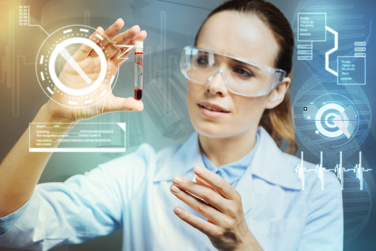 Attentive hematologist. Calm clever experienced hematologist in special glasses feeling satisfied while looking at the blood sample in her hand