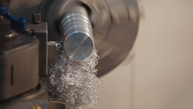 Manufacturing of metal parts on the lathe machine at the factory, lots of metal shavings, industrial concept, profile view