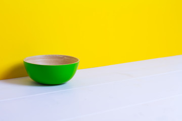 Bamboo green plate on white wooden table, yellow color paper background, paper pattern, side view, copyspace
