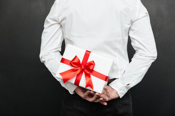Cropped image from back of man holding white present box with red bow in hands, isolated over dark gray wall