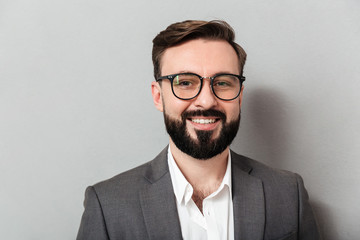 Close up portrait of caucasian unshaved man in eyeglasses looking on camera with sincere smile, isolated over gray background