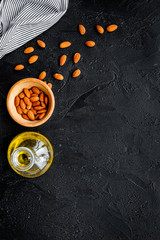 Use nut oil as cosmetics. Almond oil in jar near almond in bowl on black background top view copy space
