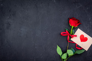 Valentine's day congratulation. Red rose and greeting card with heart sign on black background top view copy space