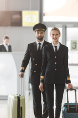 happy male and female pilots walking by airport lobby with suitcases © LIGHTFIELD STUDIOS