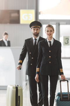 happy male and female pilots walking by airport lobby with suitcases
