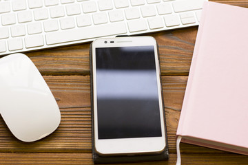 Business Office Workplace Concept with a white computer mouse, keyboard, a smartphone and a pink planner, close up, copy space