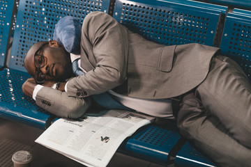 tired businessman sleeping on seats while waiting for flight at airport lobby