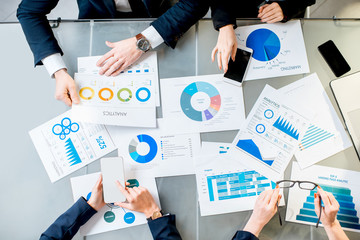 Business people working on paper charts and smartphones sitting at the table. Top view with no face
