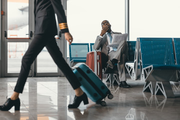 businessman waiting for flight at airport lobby while female pilot passing by