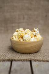 Salted popcorn in round wooden bowl on hessian fabric background, vertical style, movie night snack