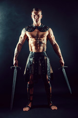 Fototapeta na wymiar Portrait of handsome muscular gladiator with two swords. Studio shot. Black background.