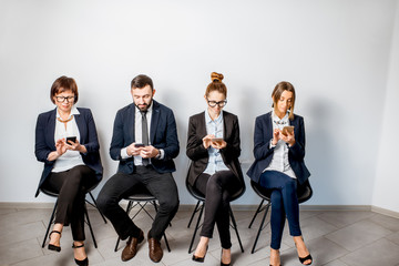 Obraz premium Business people using smart phones sitting in a row on the white wall background