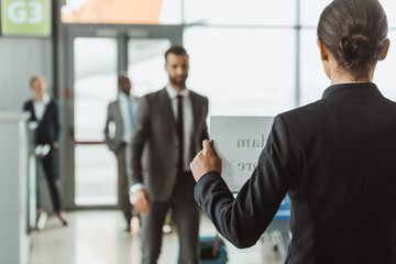businesswoman waiting for partner with name sign on paper at airport