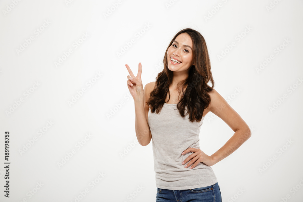 Poster smiling brunette woman with arm on hip showing peace gesture