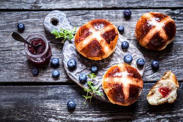 Easter hot cross buns on a wooden background with a jar of jam and fresh berries blueberry rustic