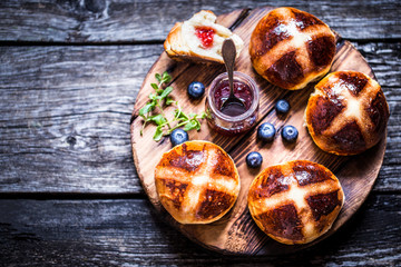 Easter hot cross buns on a wooden background with a jar of jam and fresh berries blueberry rustic