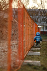 Ребёнок идёт вдоль строительного заграждения