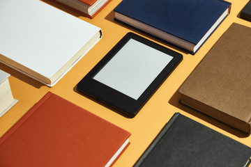 From above e-book placed in classic paper books on orange background.