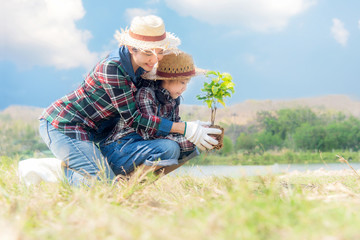 Naklejka na ściany i meble Asian Mom and child girl plant sapling tree in the nature spring for reduce global warming growth feature, reduce global warming and take care nature earth,  blue sky background. .